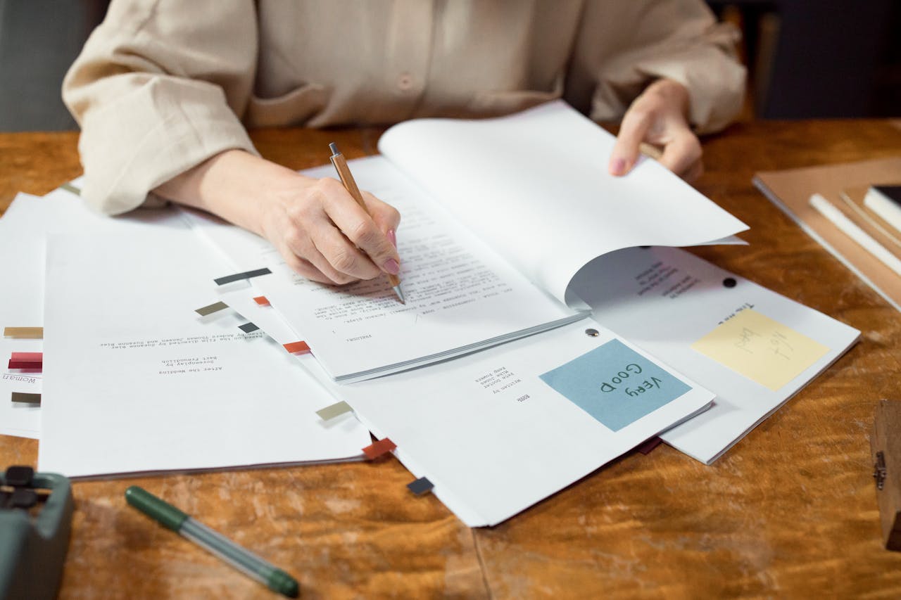 Close-up of hands writing and organizing documents on a wooden desk.